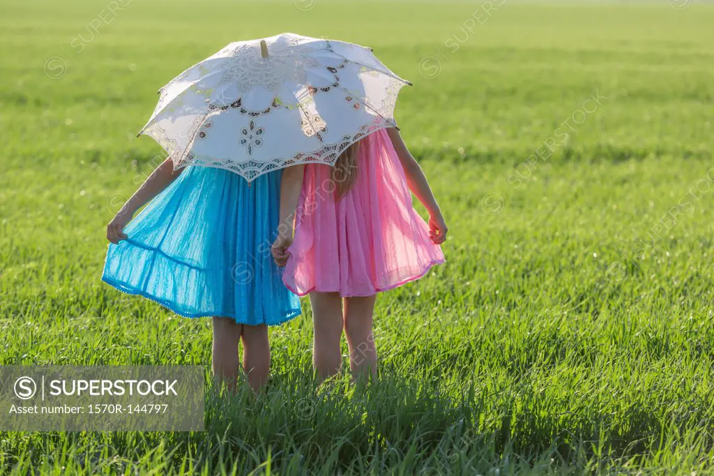 Twin sisters standing in a sunny field under an umbrella