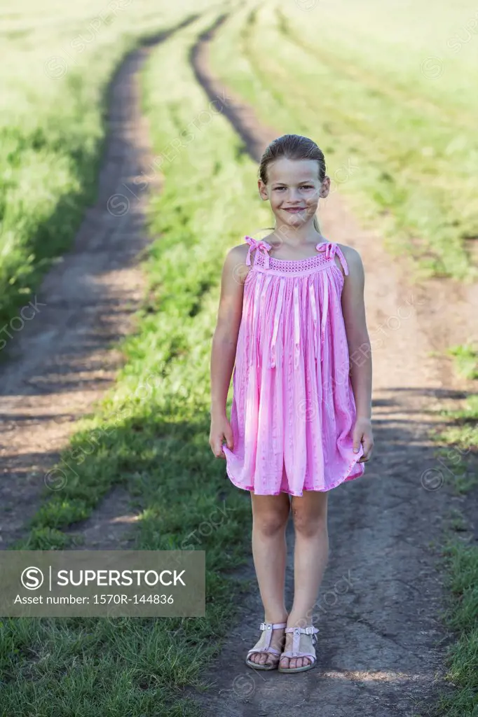 A young smiling girl standing on a dirt road in the country