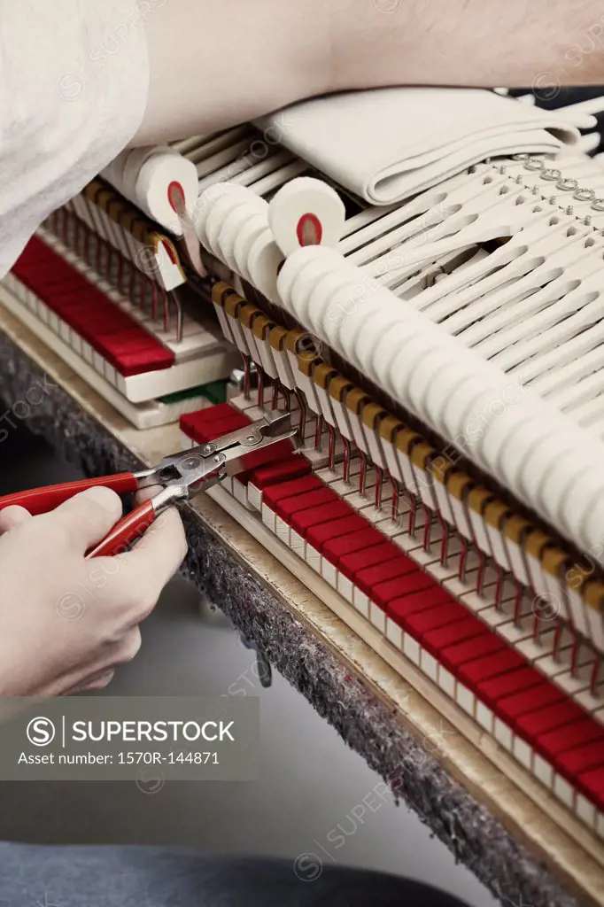 A piano repairman using pliers to fix a piano