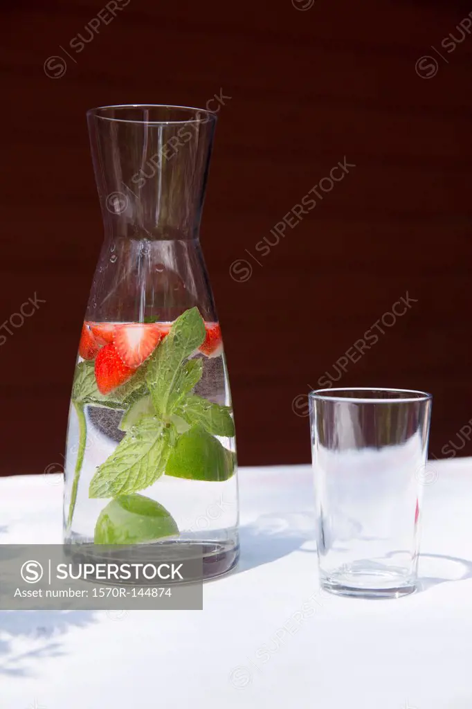 A carafe of water with sliced strawberries and mint leaves