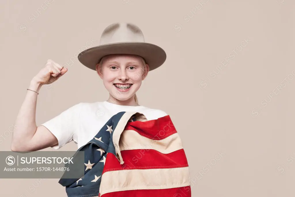 A smiling girl wearing a ranger hat wrapped in an American flag and making a fist