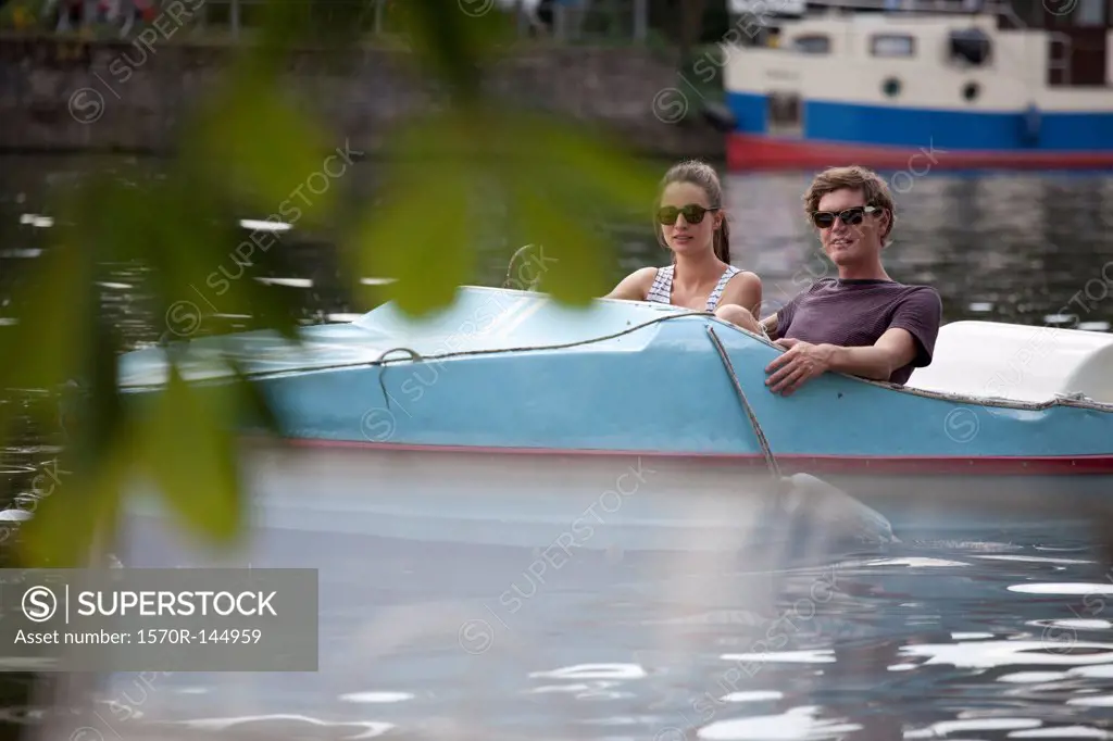 Young couple riding paddle boat on lake