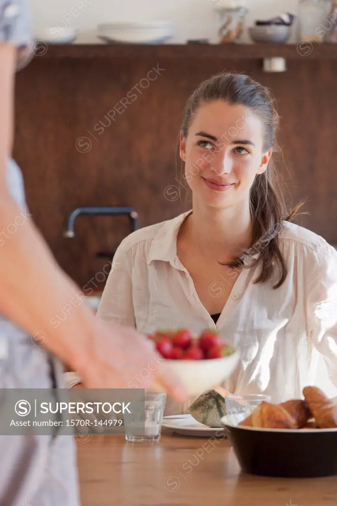 Young woman sitting at dining table with breakfast, smiling