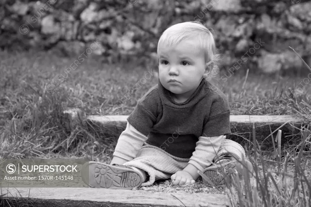 Baby boy sitting on ground, looking away