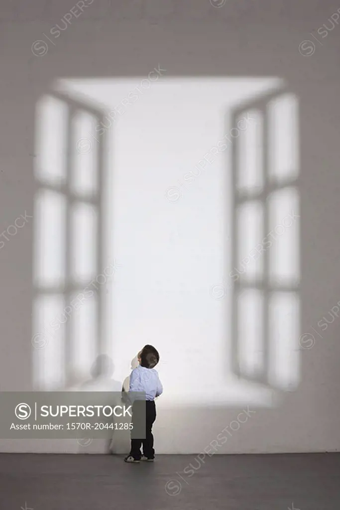 Boy looking at shadow of open window on white wall at home