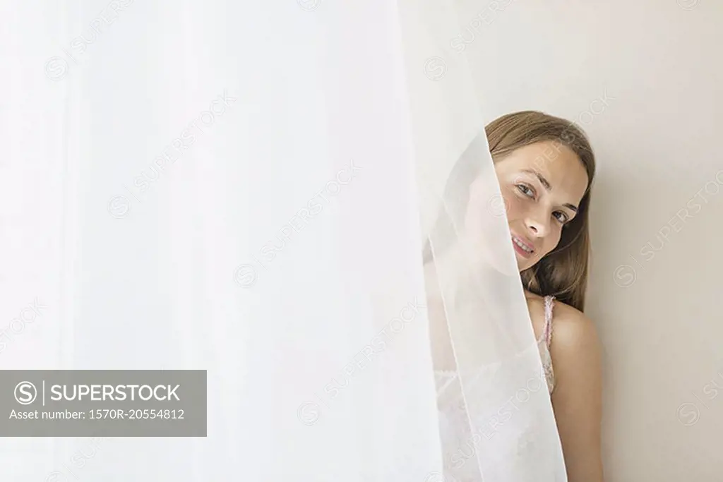 Portrait of smiling woman hiding behind curtain at home