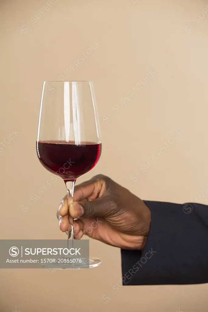 Cropped hand holding red wineglass against colored background