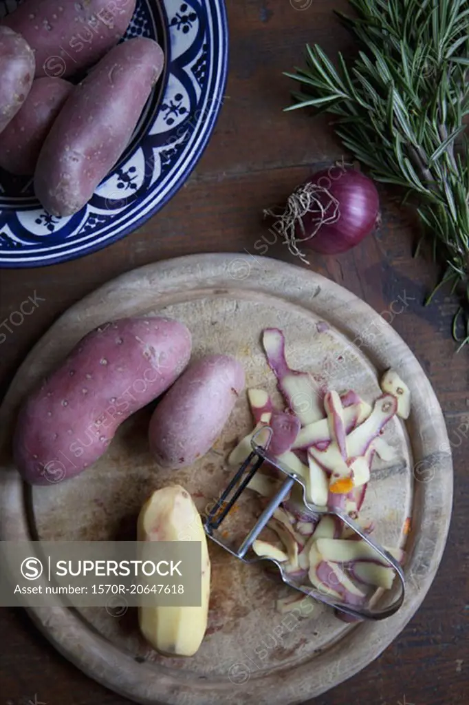 Directly above shot of potatoes with peeler on cutting board