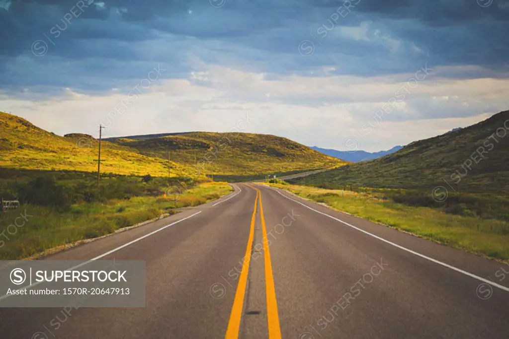 Road leading towards green mountains against cloudy sky