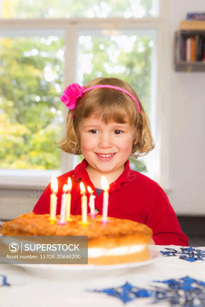 Happy girl looking at birthday cake on table