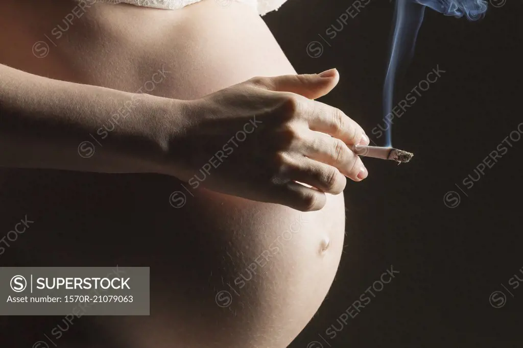 Midsection of pregnant woman smoking cigarette against gray background