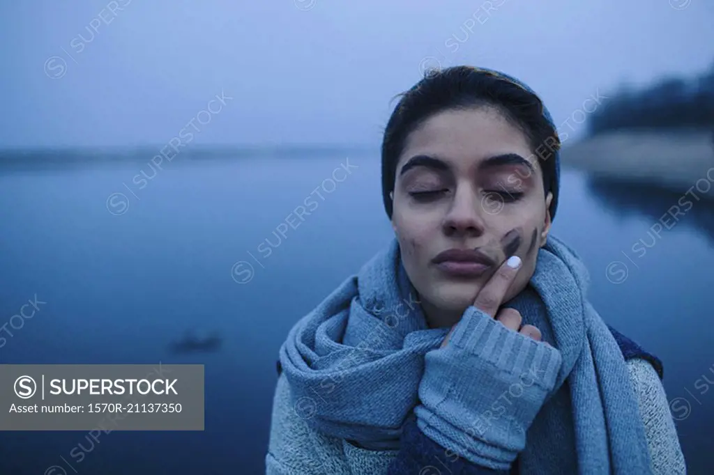 Teenage girl touching dirt covered face against lake
