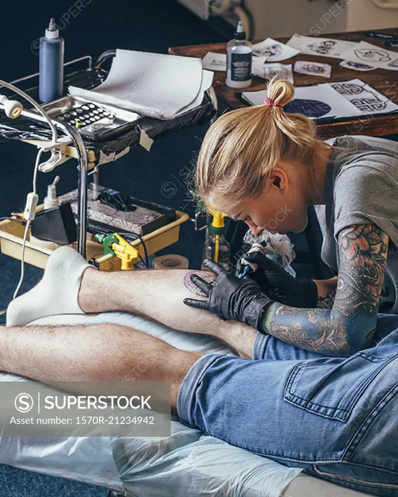 Artist tattooing design on man's leg at studio