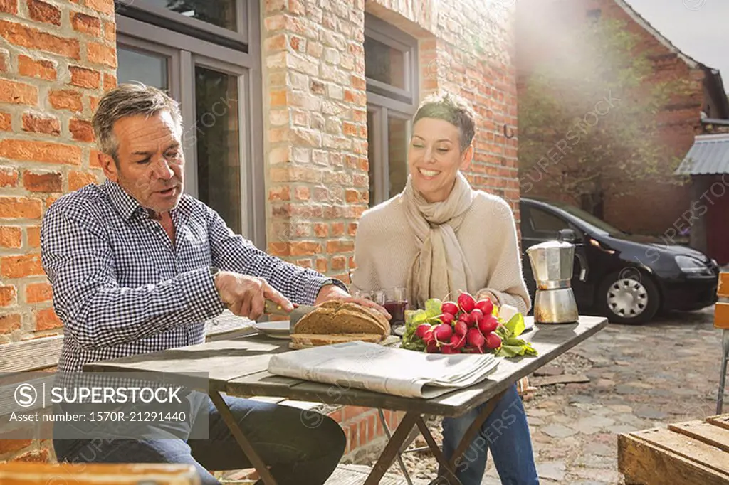 Woman looking at man slicing bread in back yard