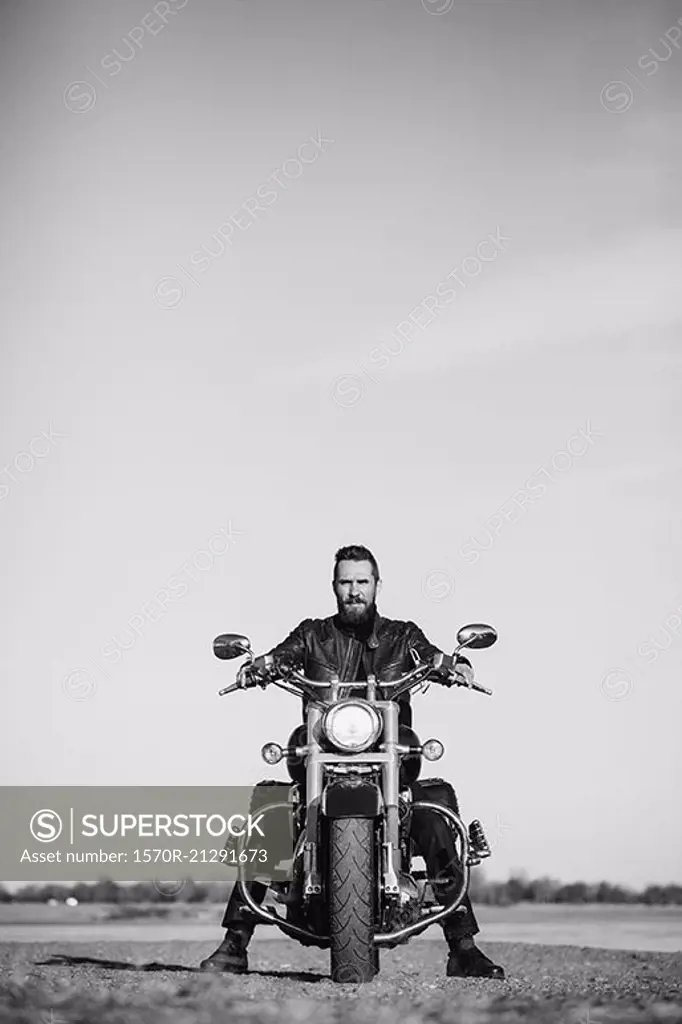 Full length portrait of biker sitting on motorcycle against clear sky