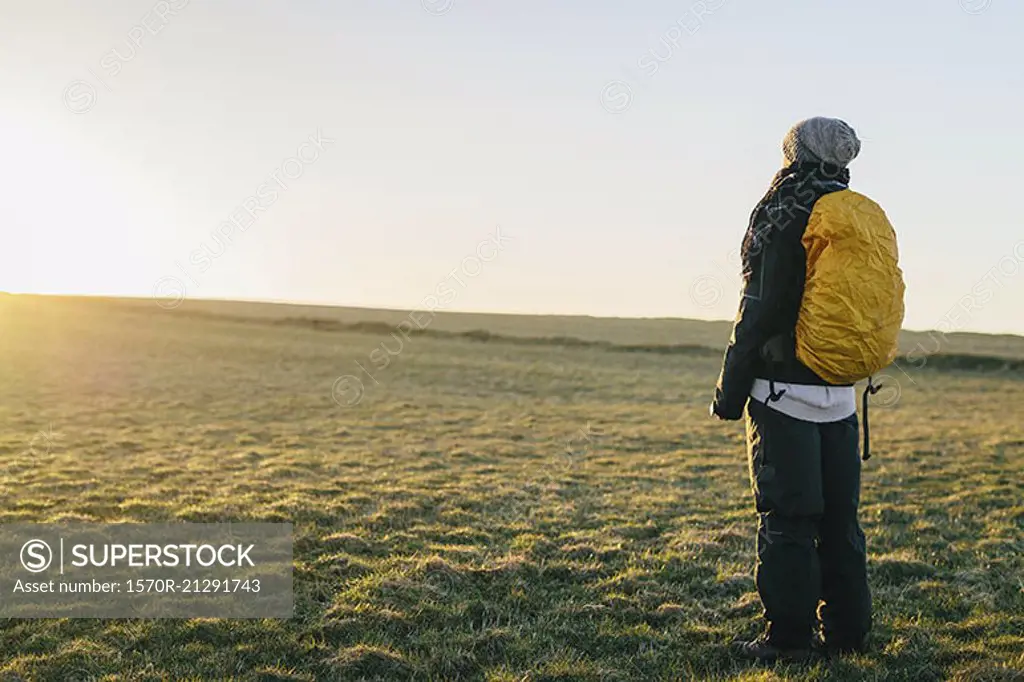 Rear view of female hiker standing on field against clear sky during sunrise