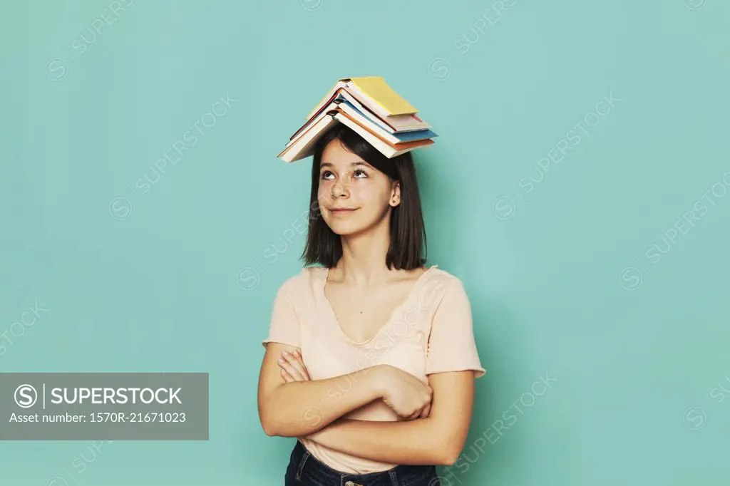 Smiling girl balancing book with arms crossed against turquoise background