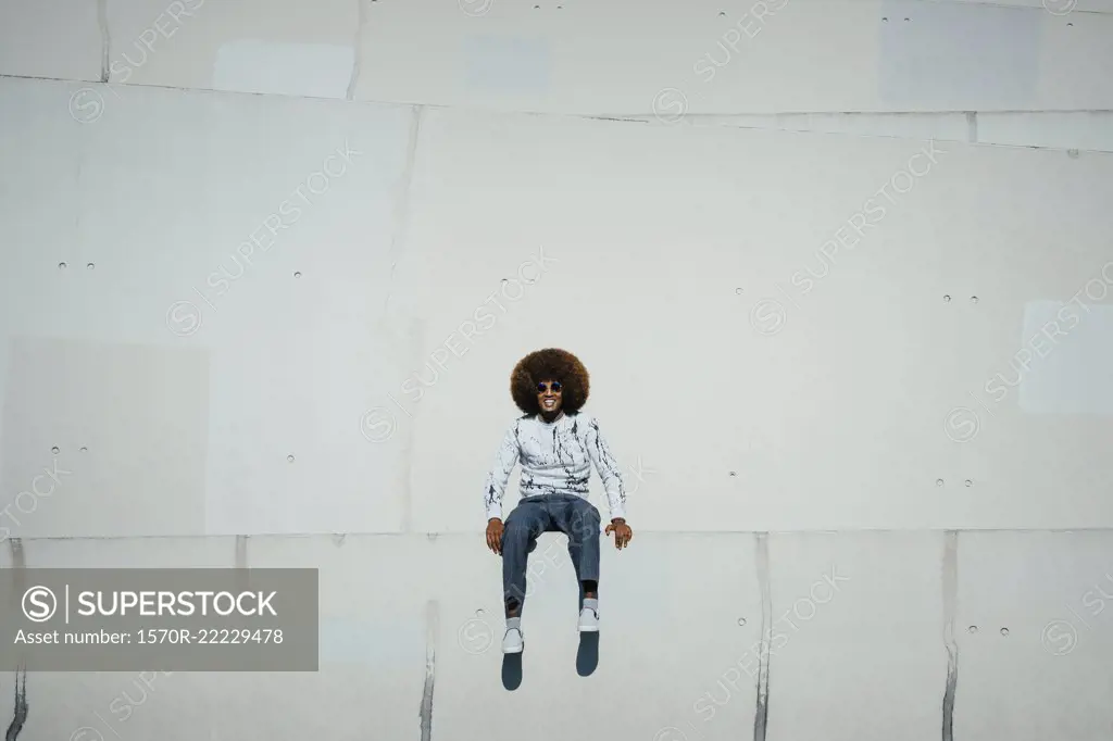 Portrait happy young man with afro sitting on wall