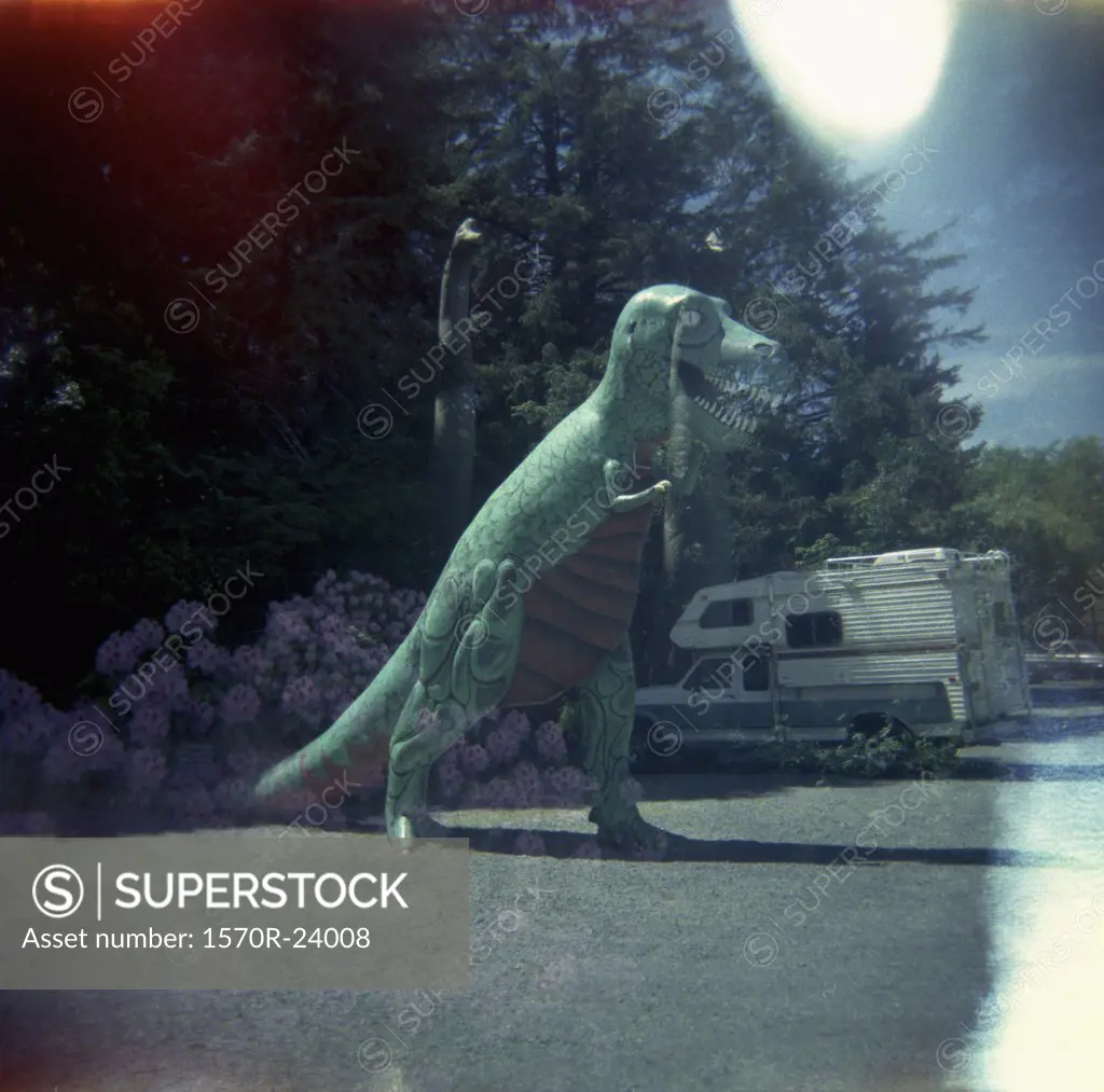 A statue of a dinosaur in a parking lot next to a camper