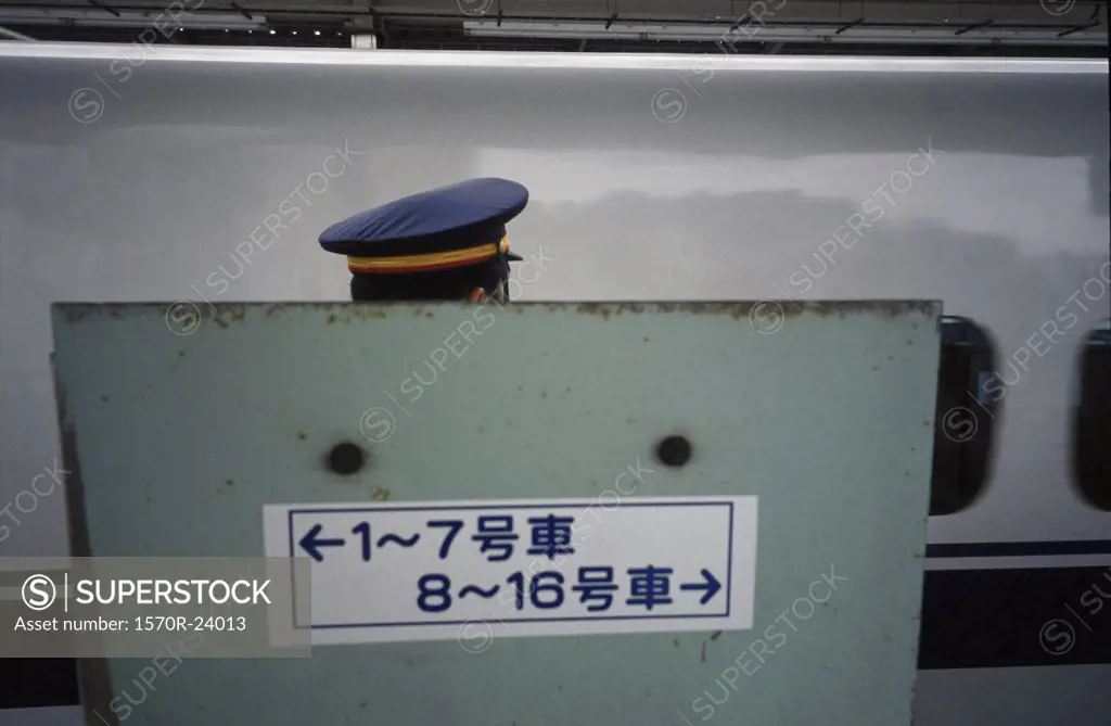 A train conductor between a sign with Japanese writing and a train