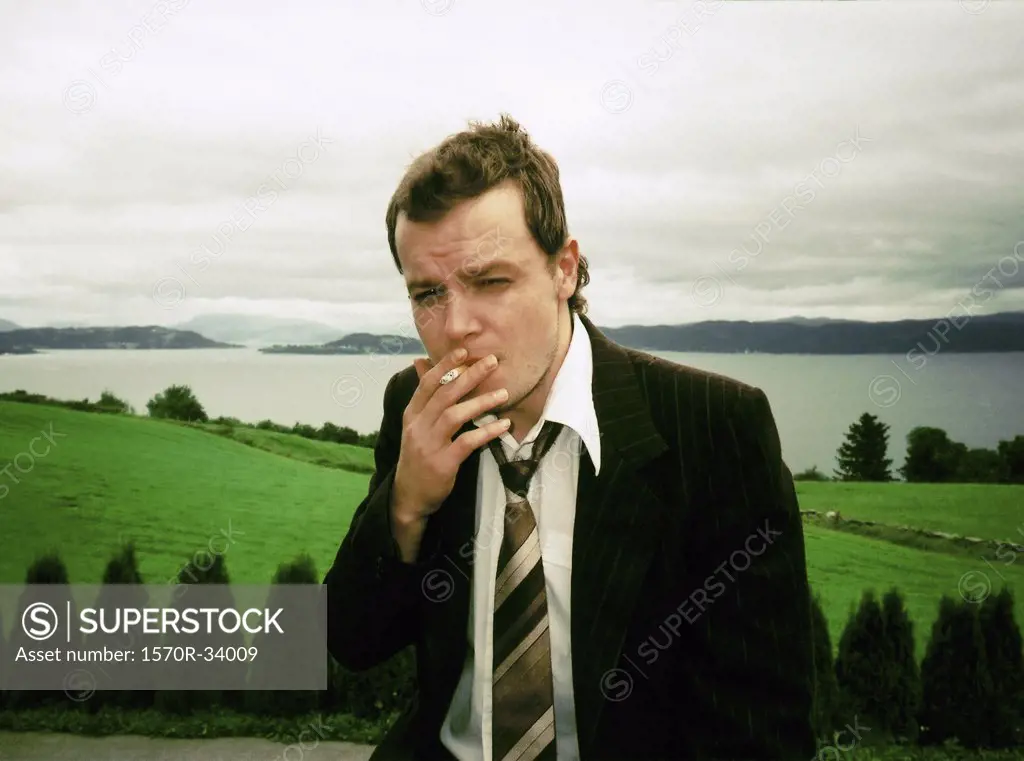 Man smoking a cigarette in front of countryside landscape