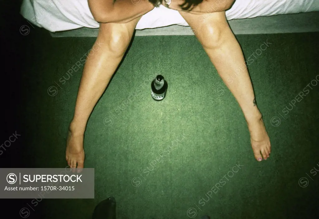 Aerial view of a person sitting on a bed with a beer bottle between his legs