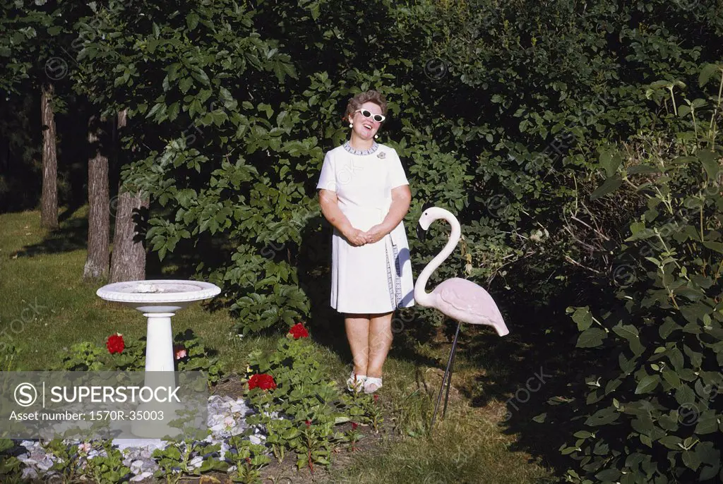 A woman standing in a garden next to a statue of a pink flamingo