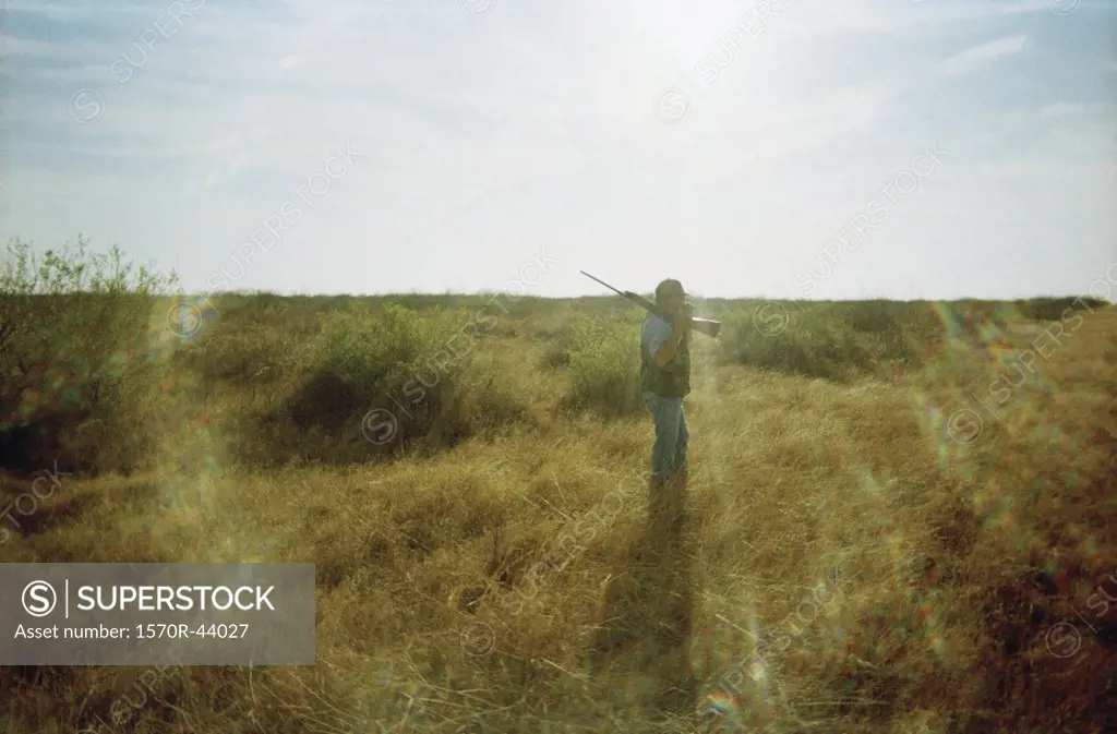 A person with a gun walking through a field