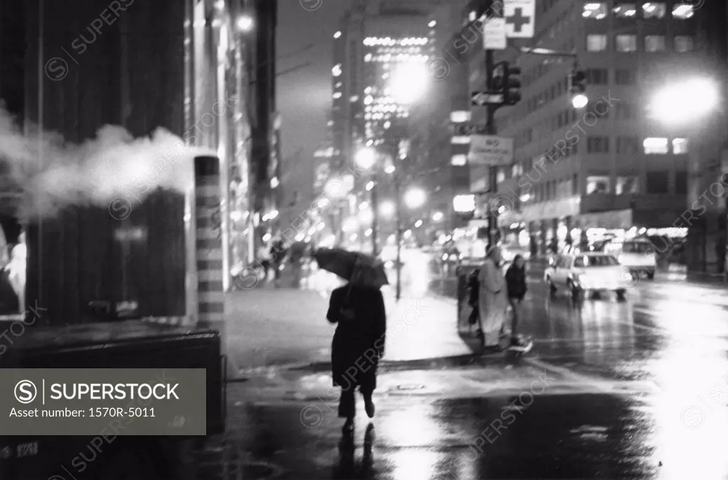 A person crossing a New York city street with an umbrella at night