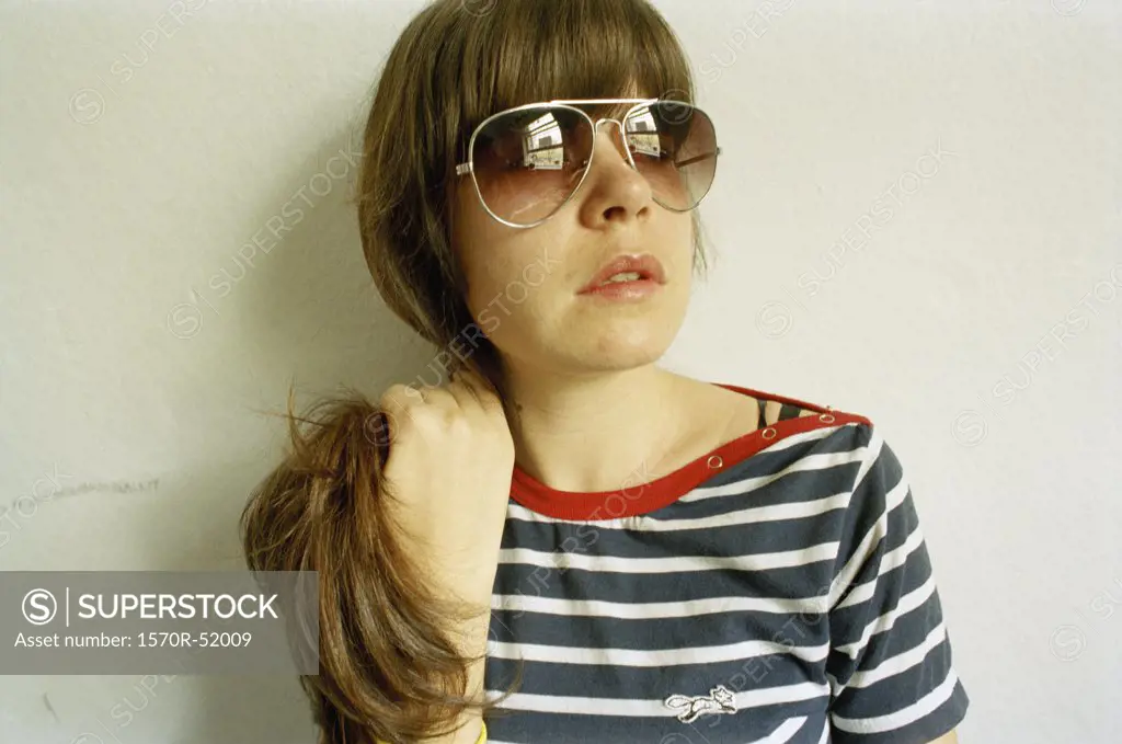 A young woman wearing sunglasses holds her hair back