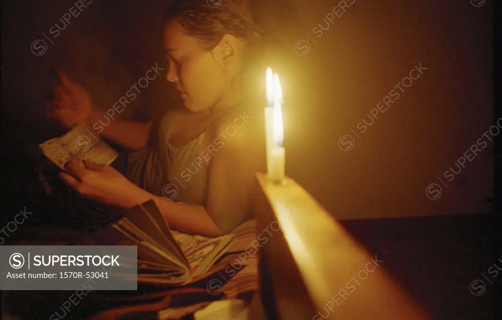 A young woman reading by candlelight