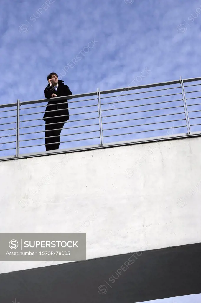 A businessman leaning on a railing with a mobile phone
