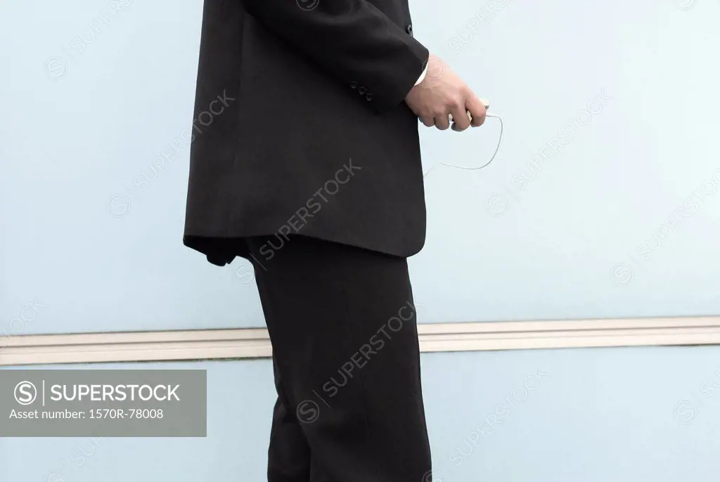 A businessman standing next to a wall holding a portable music player