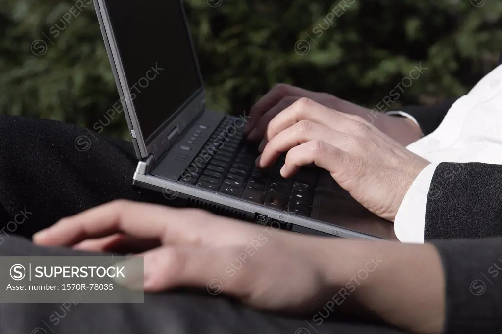 A businessman typing on a laptop computer next to a businesswoman 