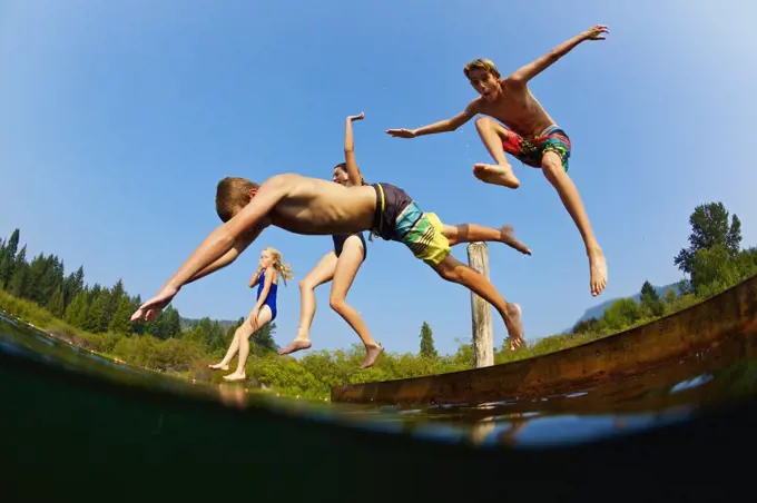 Playful kids jumping off dock into sunny summer lake