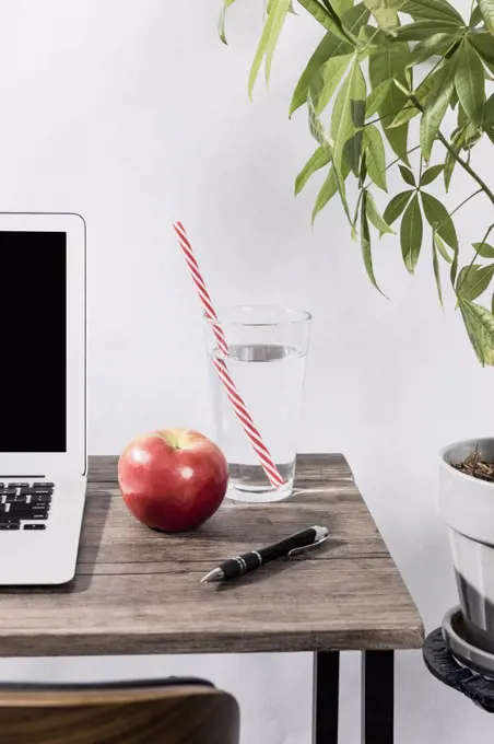 Water, apple and pen on desk next to laptop in office