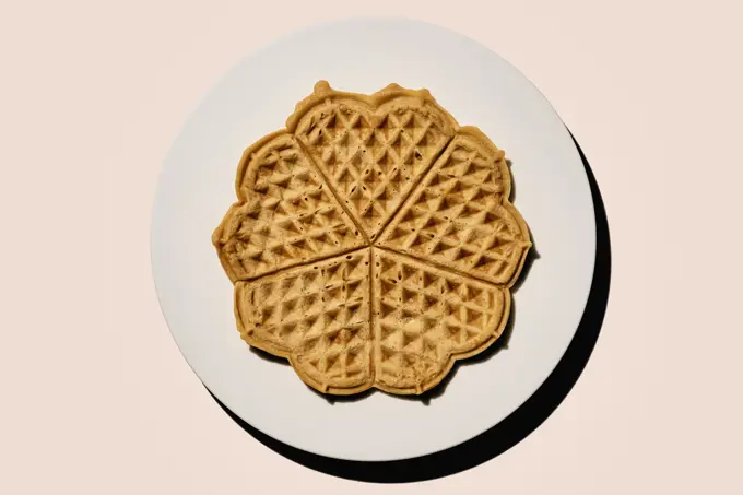 Still life scalloped heart-shape waffles on plate on pink background