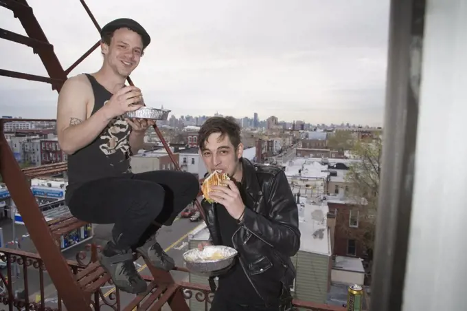 Two young men eating take out food on a fire escape
