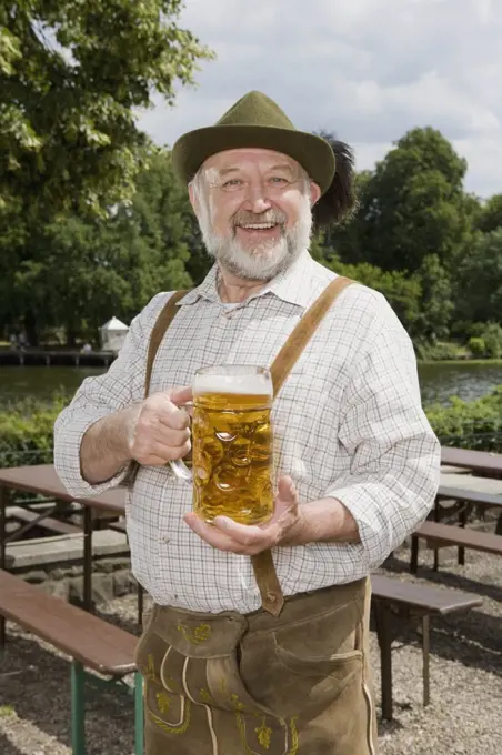 A traditionally clothed German man in a beer garden holding a beer glass 