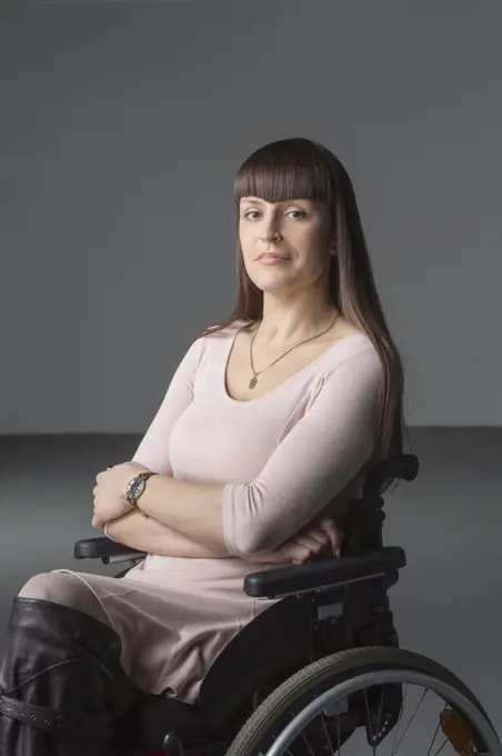 Portrait of confident disabled woman in wheelchair against gray background
