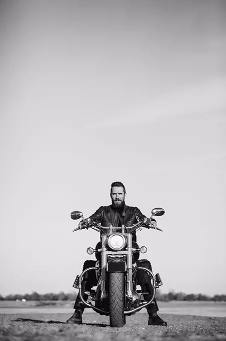 Full length portrait of biker sitting on motorcycle against clear sky