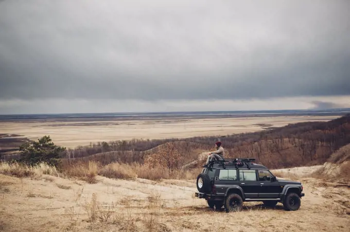Distant man sitting on top of sports utility vehicle at field against cloudy sky, Amur, Russia
