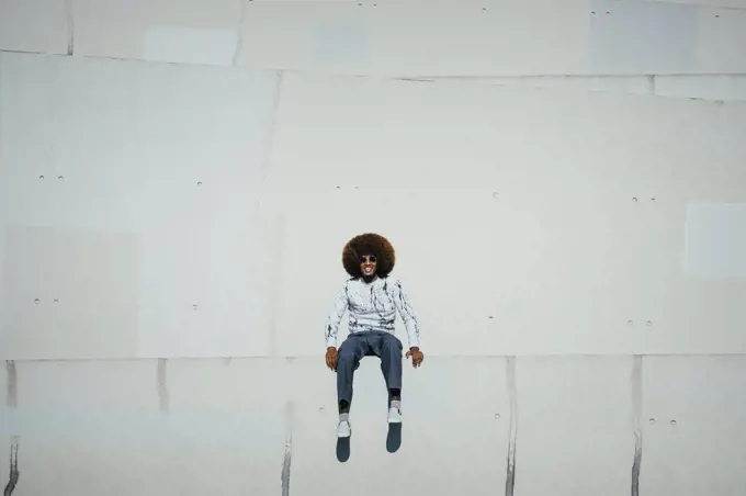 Portrait happy young man with afro sitting on wall