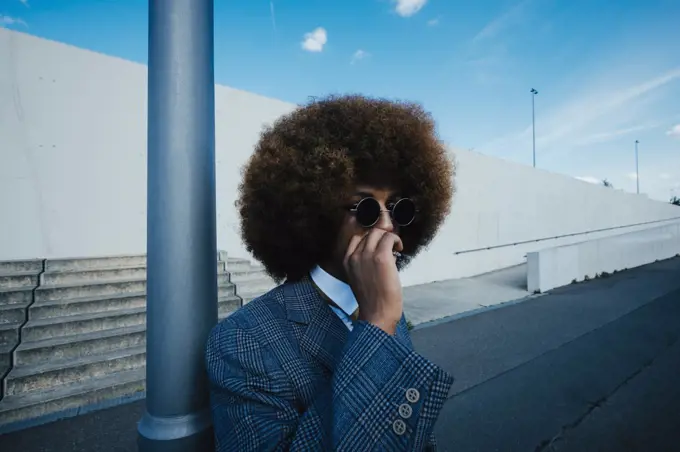 Well-dressed young man with afro smoking cigarette on urban sidewalk