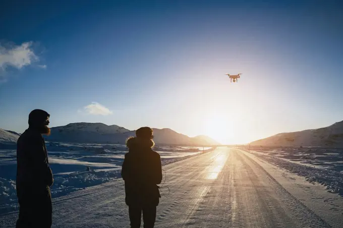 Father and son flying drone over remote, snow covered road, Reykjadalur, Iceland