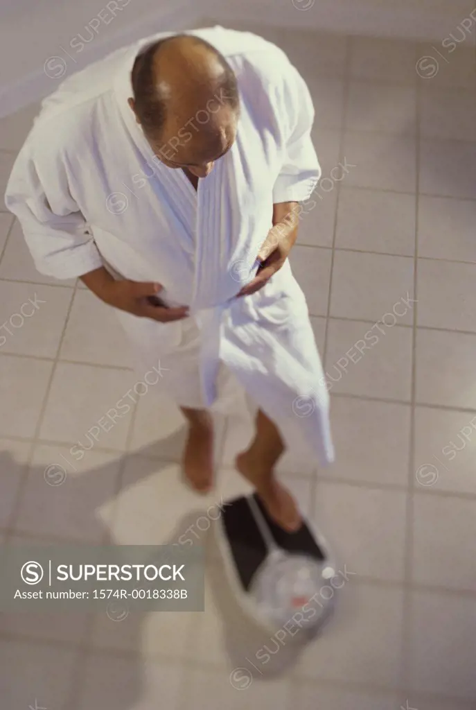High angle view of a senior man standing on a weighing scale in the bathroom