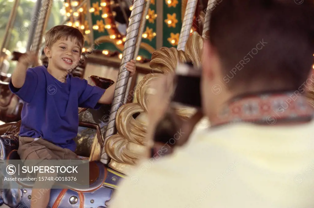 Rear view of a father taking a photograph of his son riding a carousel horse