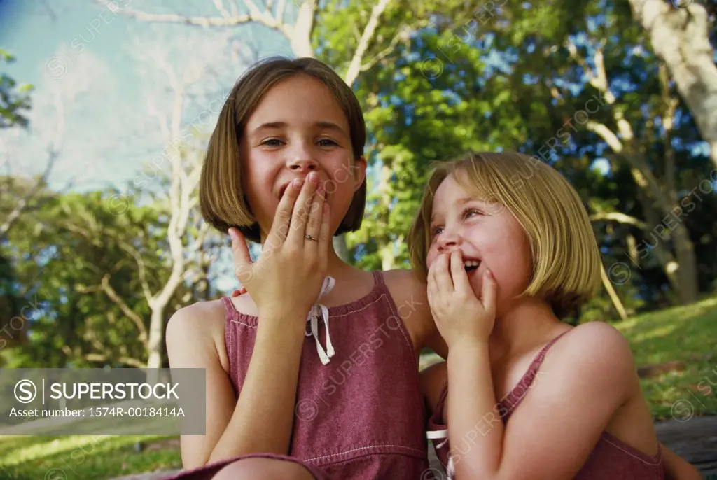 Low angle view of two girls smiling and covering their mouths with their hands
