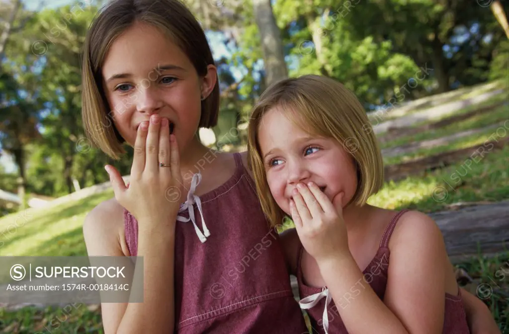 Portrait of two smiling girls with their hands over their mouths
