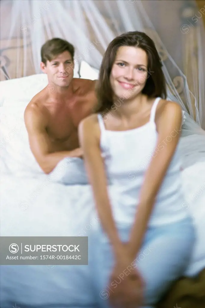 Portrait of a young woman smiling with a young man sitting behind her on a bed